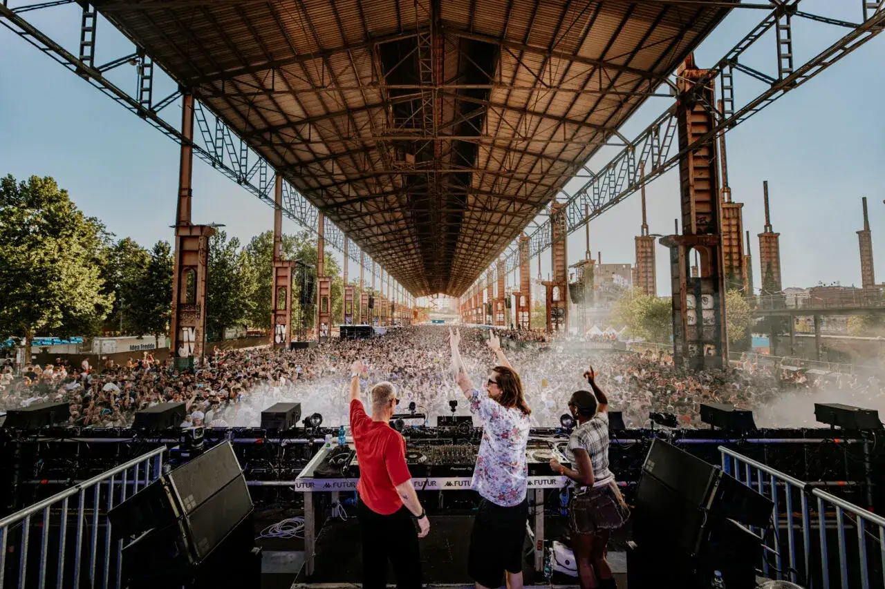 DJ set al futur festival, con una folla immensa che balla sotto una struttura industriale.