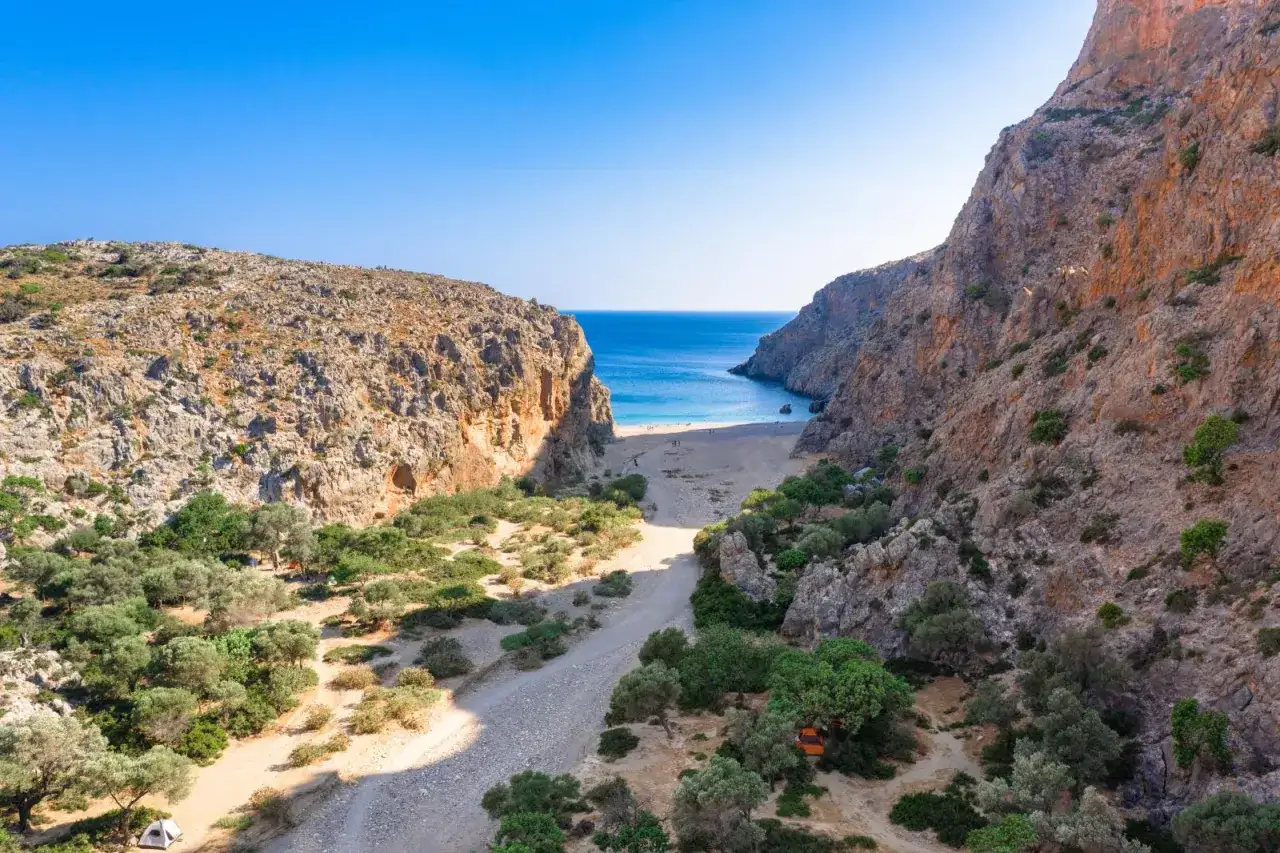 Eine beeindruckende Schlucht auf Kreta führt zu einem einsamen Strand am türkisfarbenen Meer. Olivenbäume säumen den Weg.