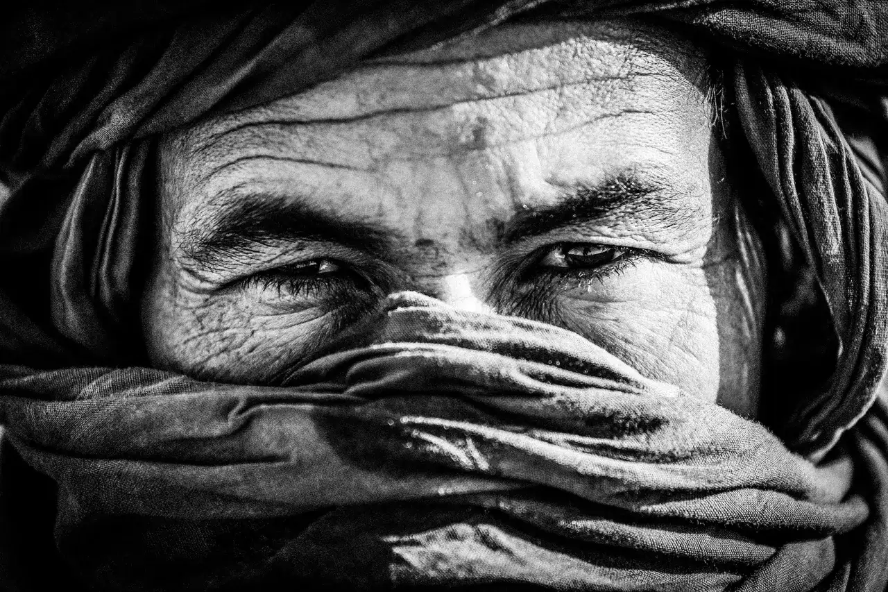Portrait monochrome d'un homme voilé, ses yeux perçants fixent l'objectif, le tissu cache sa bouche.