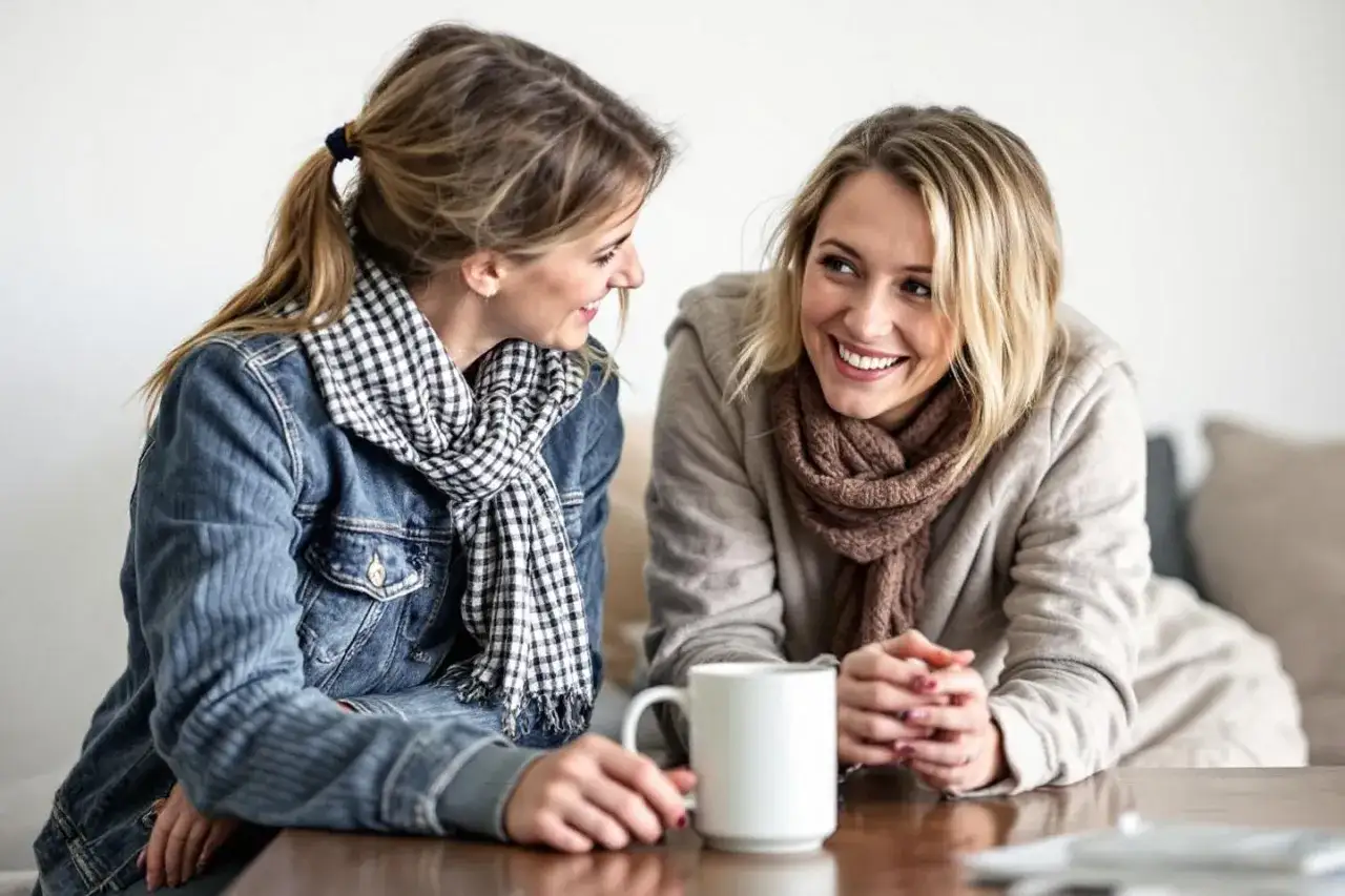 Två kvinnor ler mot varandra över en kaffekopp. De har på sig varma kläder och halsdukar, en fin påminnelse om att respektera varandra.