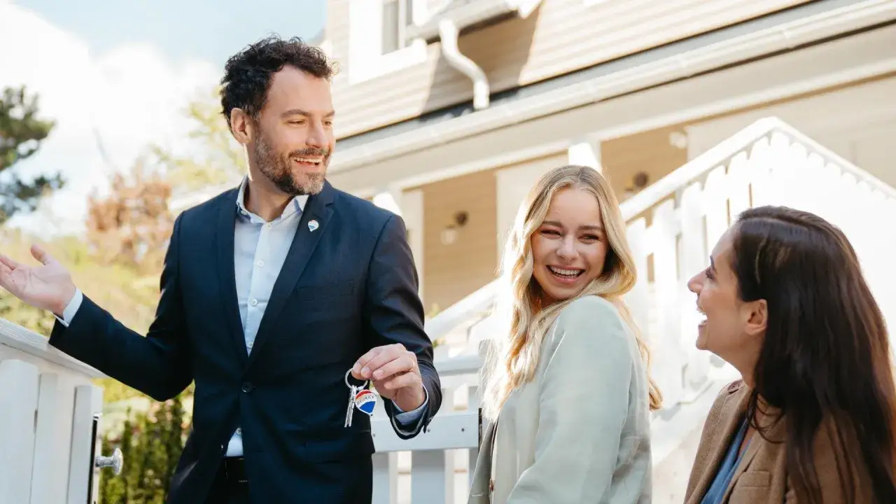 Agente immobiliare consegna le chiavi a una giovane coppia felice. Ecco come comprare casa con successo!