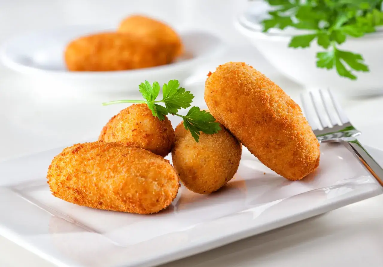 Quatre croquettes de crevette dorées et croustillantes, garnies de persil frais, sur une assiette blanche.