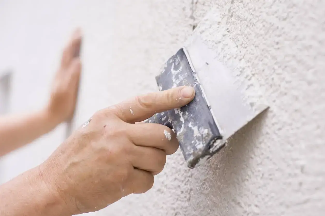 Mano aplicando masa con espátula para reparar gotele en pared texturizada.
