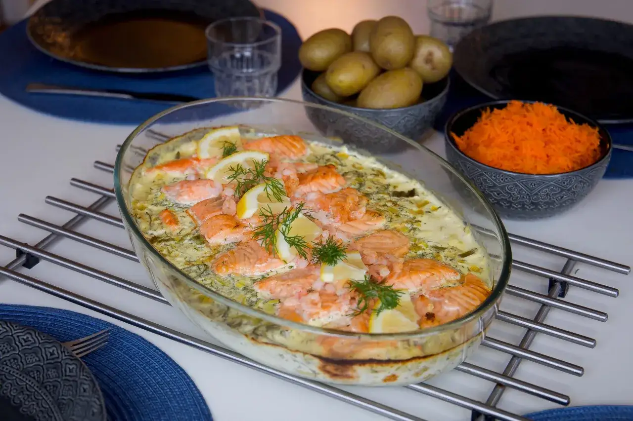 En ugnsbakad laxrätt med krämig sås till laxen, garnerad med citron och dill. Serveras med kokt potatis och riven morot.