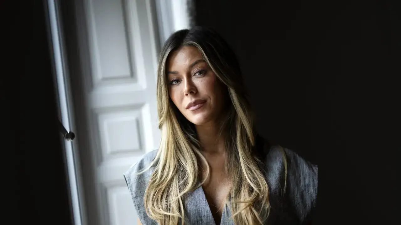 Bianca Ingrosso, med sitt blonda hår och grå klänning, poserar framför en dörr. Kanske väntar hon på sin partner.