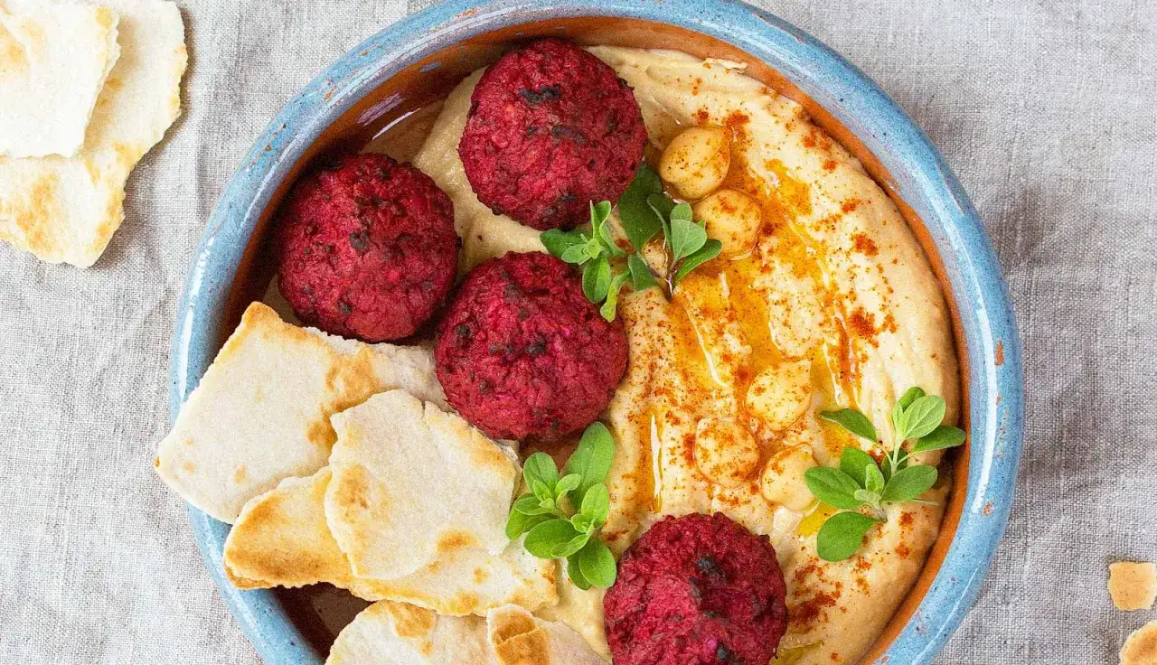 Rote Bete Falafel auf cremigem Hummus, garniert mit Kichererbsen, Kr&auml;utern und Paprikapulver. Dazu Fladenbrot.