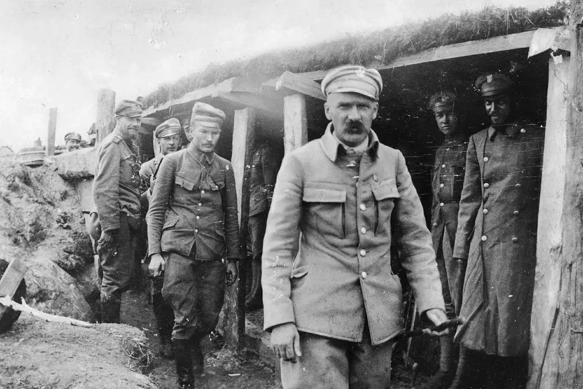 Żołnierze w okopach, w tym oficer z wąsami, w mundurach nawiązujących do tradycji **Legionów Polskich**.
