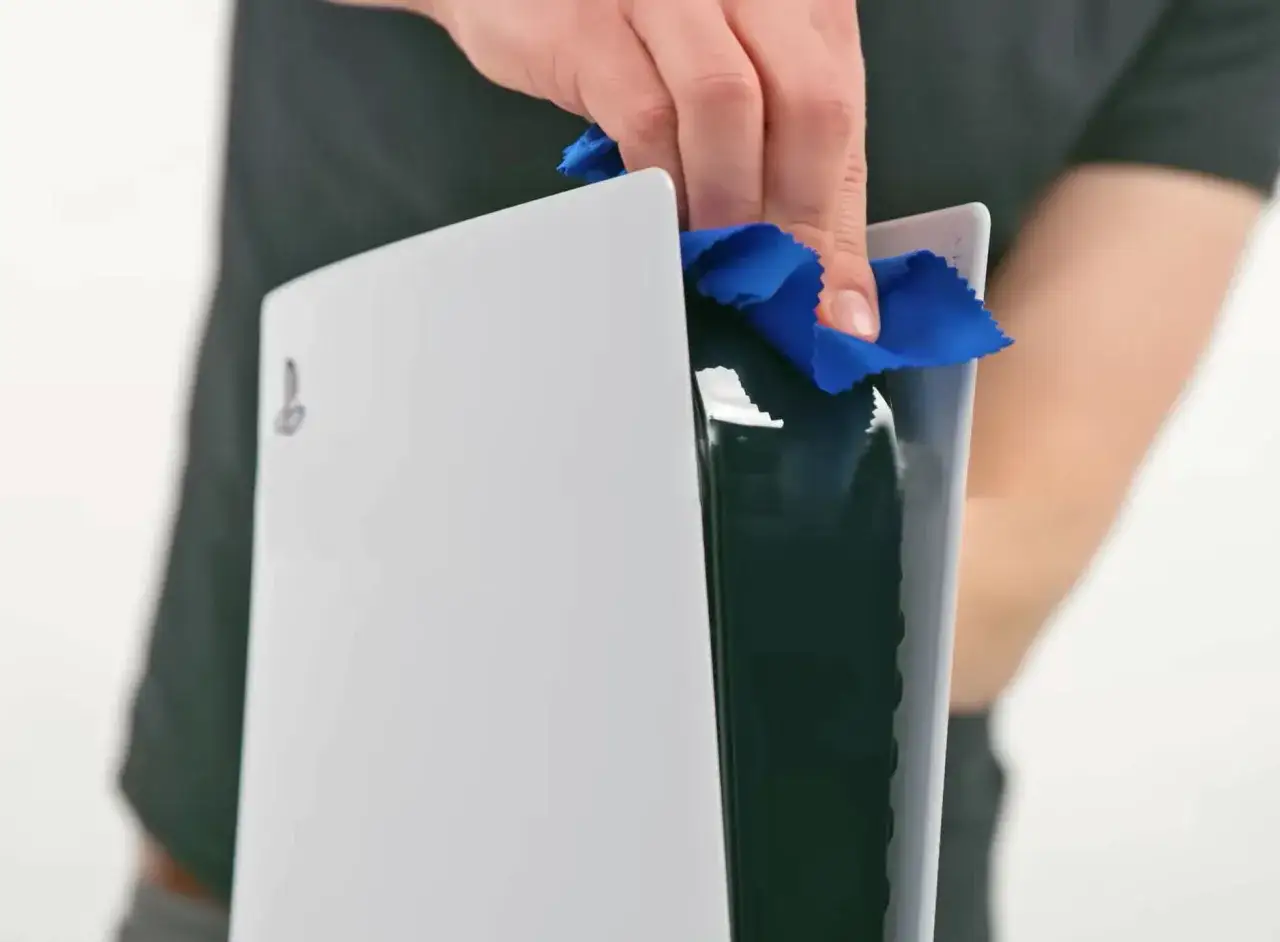 Eine Hand reinigt die PS5 mit einem blauen Mikrofasertuch. So bleibt deine Konsole staubfrei und leistungsfähig.