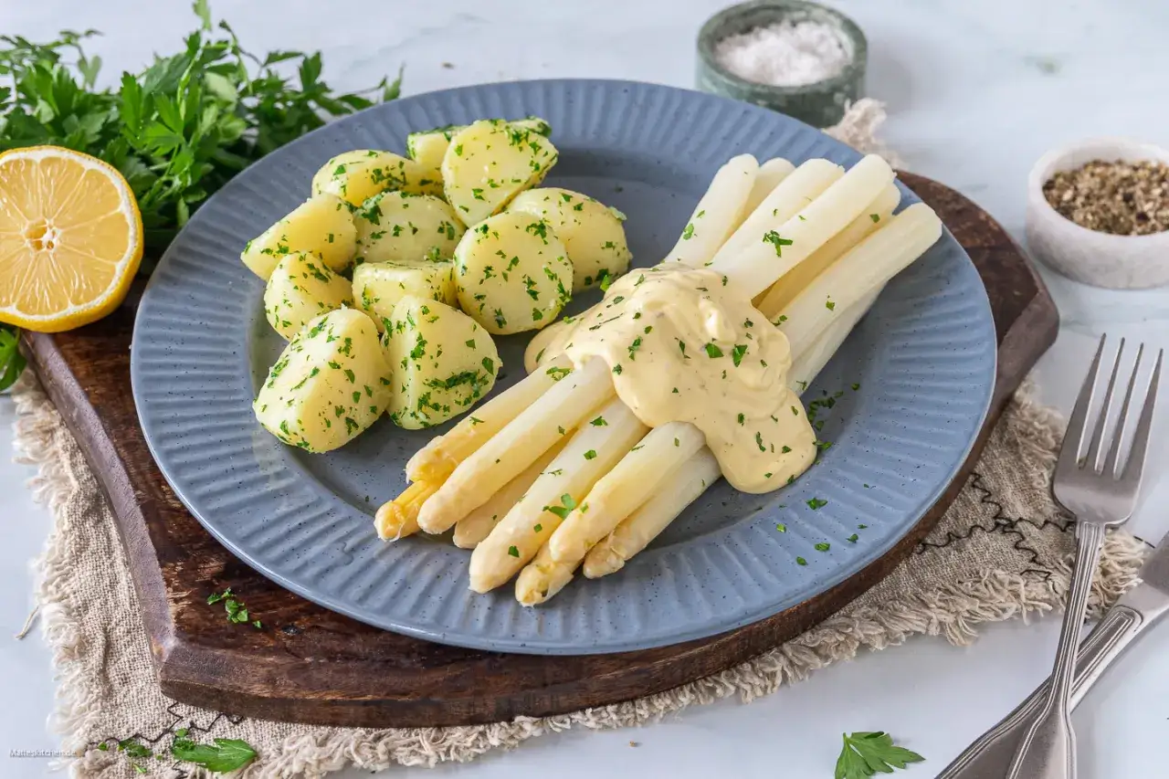 Frischer weißer Spargel, perfekt gekocht, mit Sauce Hollandaise und Petersilienkartoffeln auf einem blauen Teller.
