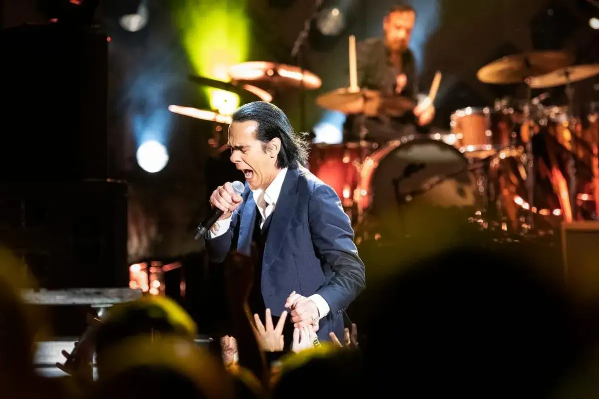 Nick Cave sjunger passionerat under en konsert, publiken sträcker sig upp. En oförglömlig kväll på Nick Cave tour.