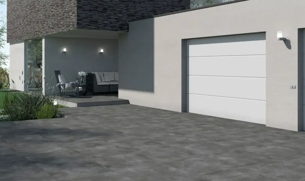Viali moderni con lastre cemento carrabili grigie, che conducono a un garage bianco e un'area esterna con divani.