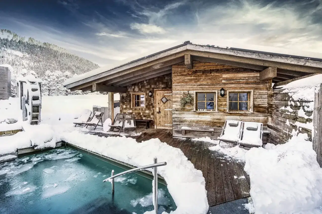 Holzh&uuml;tte mit Pool und Liegest&uuml;hlen, bedeckt von Schnee. Ein idyllisches Bild von Bayern im Winter.