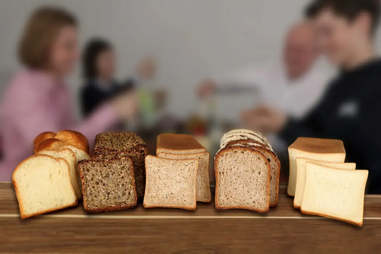 Une variété de pains, dont du pain au son, est présentée sur une table en bois. Au fond, une famille est floue.