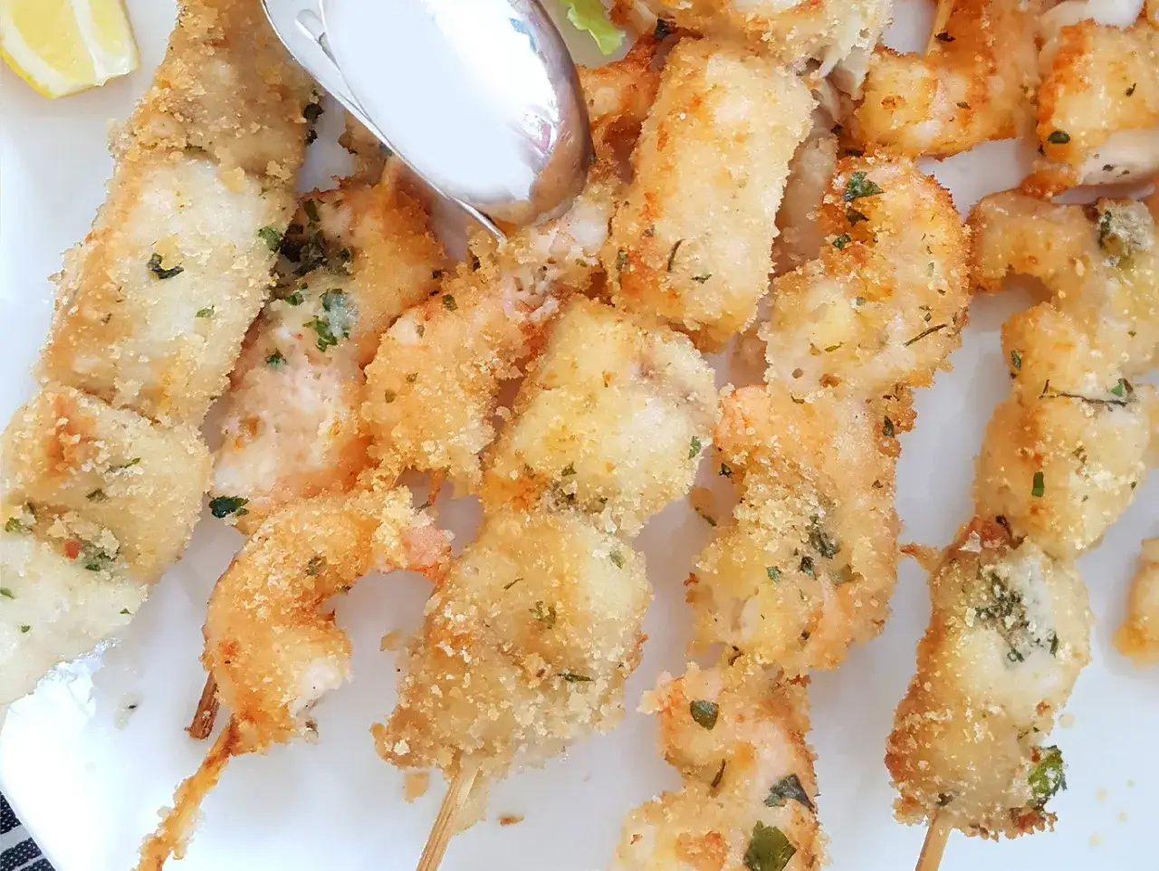 Spiedini di pesce dorati e croccanti, con gamberi e cubetti di pesce, guarniti con prezzemolo. Un piatto invitante, pronto per essere gustato.