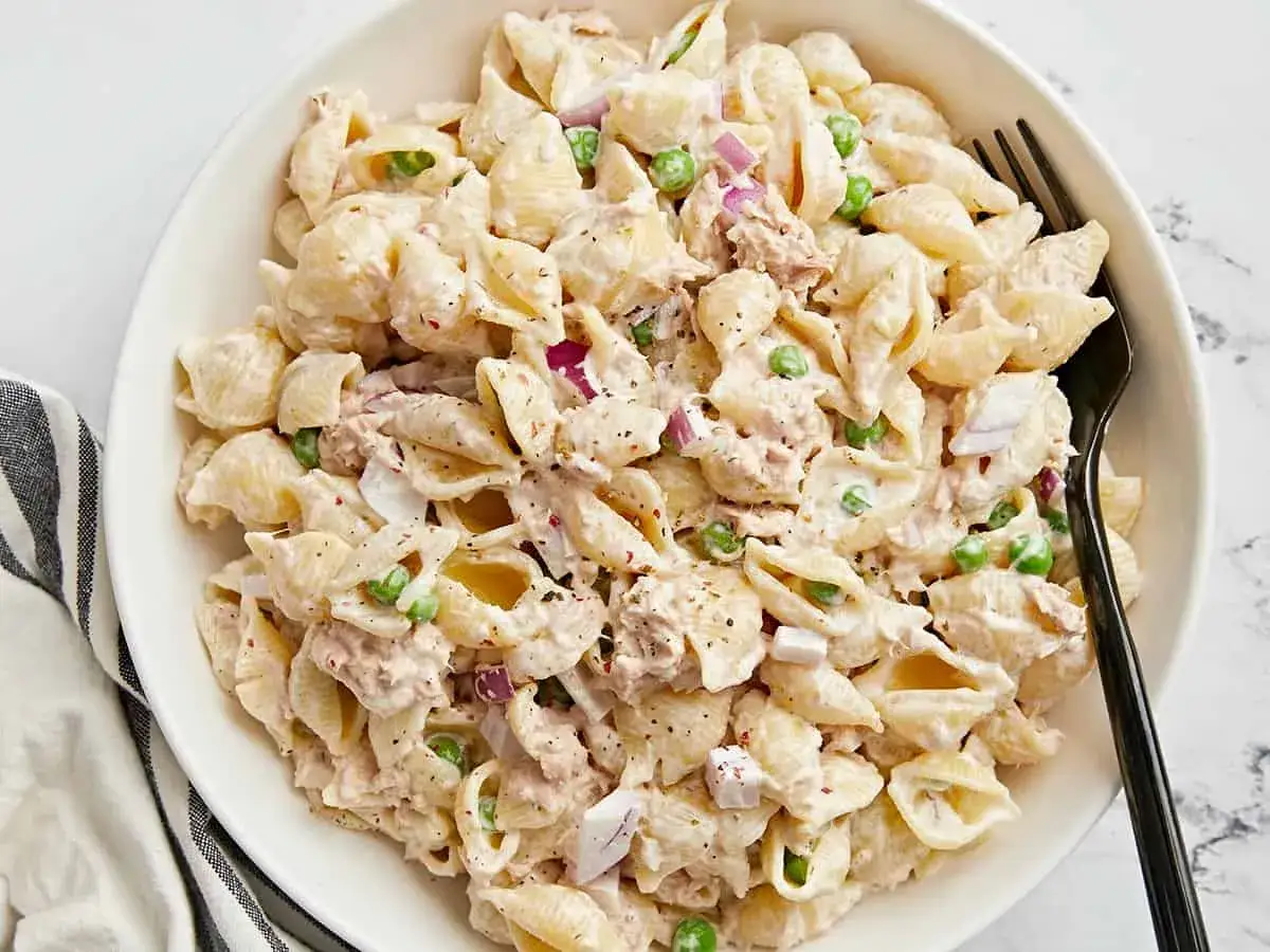 Cremiger nudelsalat mit thunfisch, Erbsen und roten Zwiebeln in einer weißen Schüssel, bereit zum Servieren.