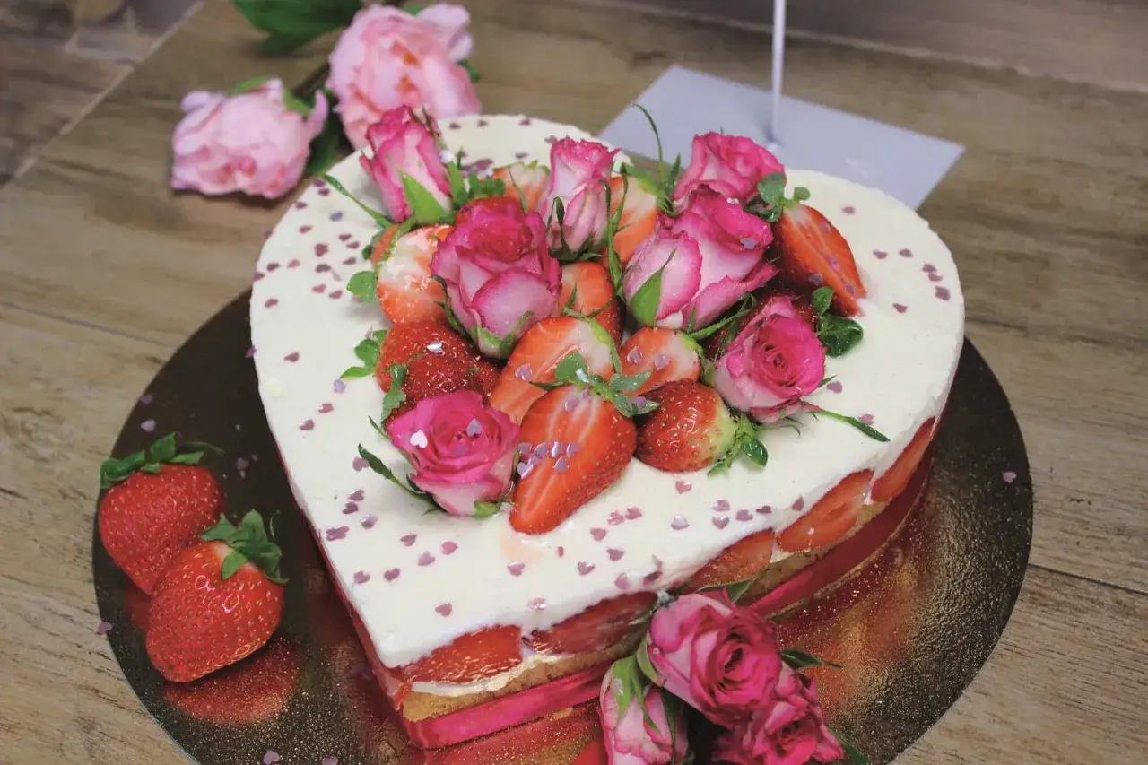 Herzförmiger Muttertagskuchen mit frischen Erdbeeren und Rosen. Ein süßer Genuss, der Liebe und Wertschätzung ausdrückt.