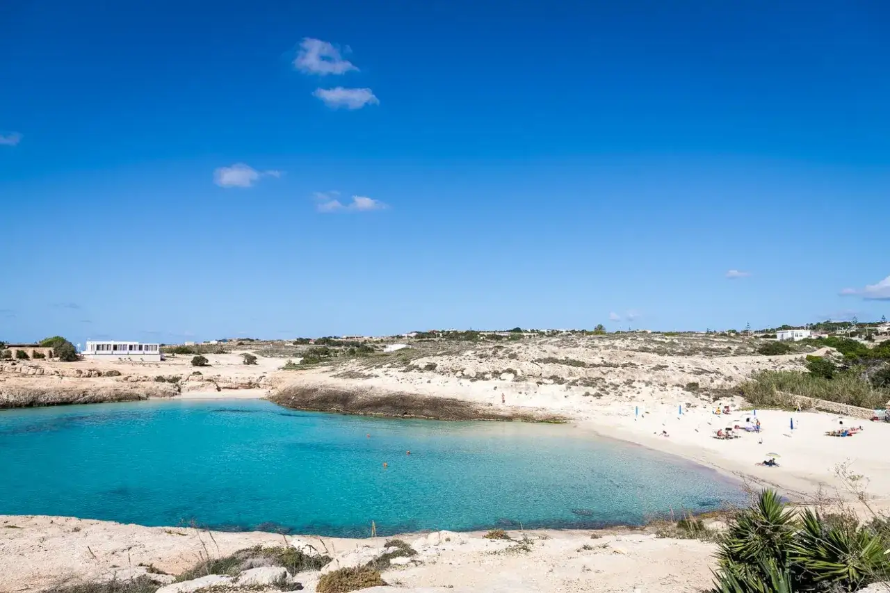 Acque cristalline e sabbia dorata a Cala Croce, Lampedusa. Un angolo di paradiso sotto un cielo azzurro intenso.
