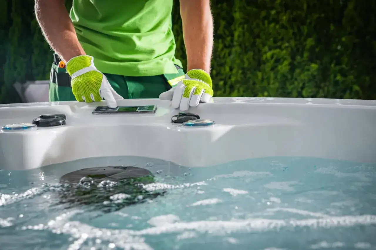 Osoba w zielonej koszulce i rękawiczkach dotyka panelu sterowania jacuzzi, sprawdzając poziom chemii.