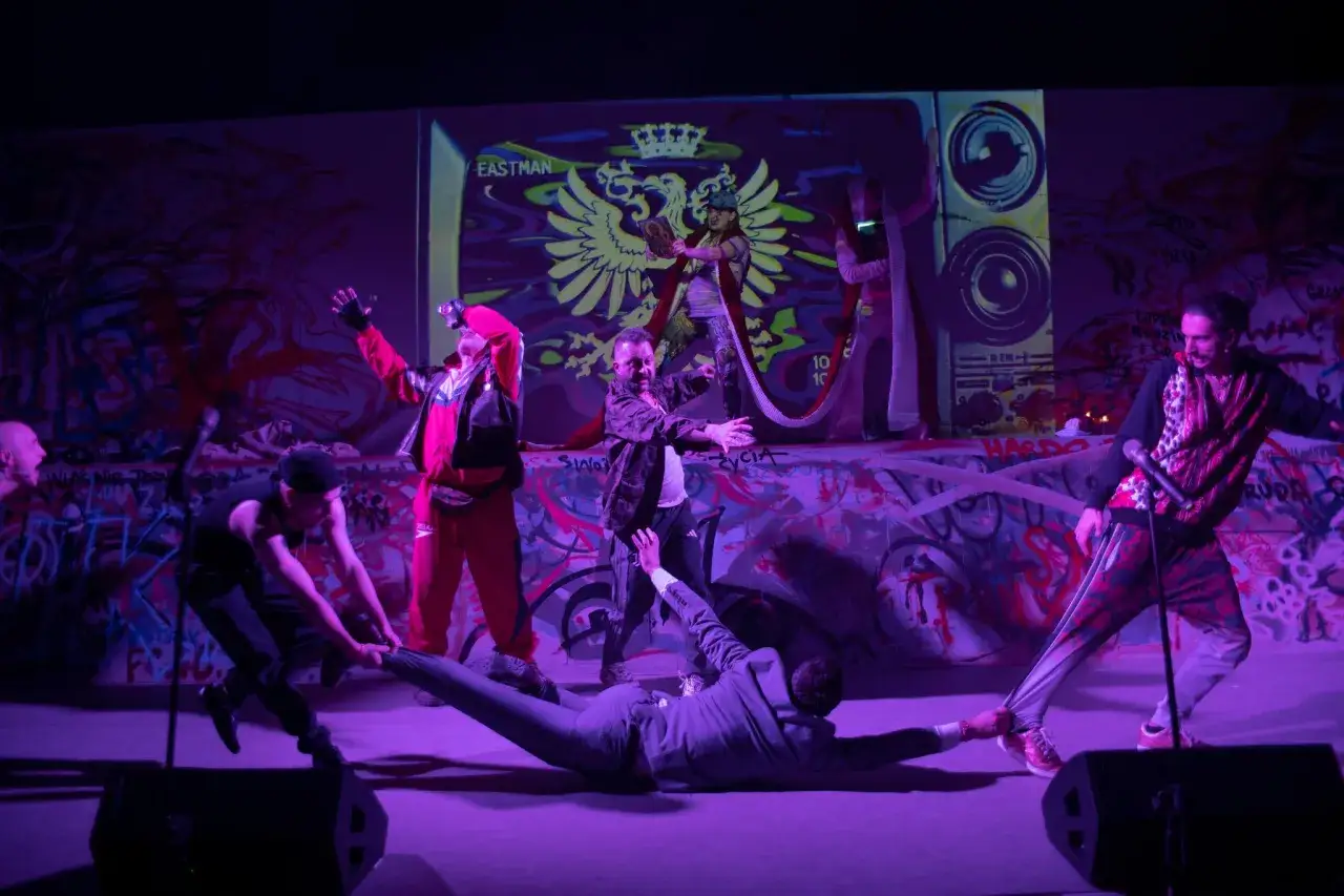 Energetyczni performers, co to za scena! Tancerze w neonowych strojach i garniturze na scenie z graffiti.