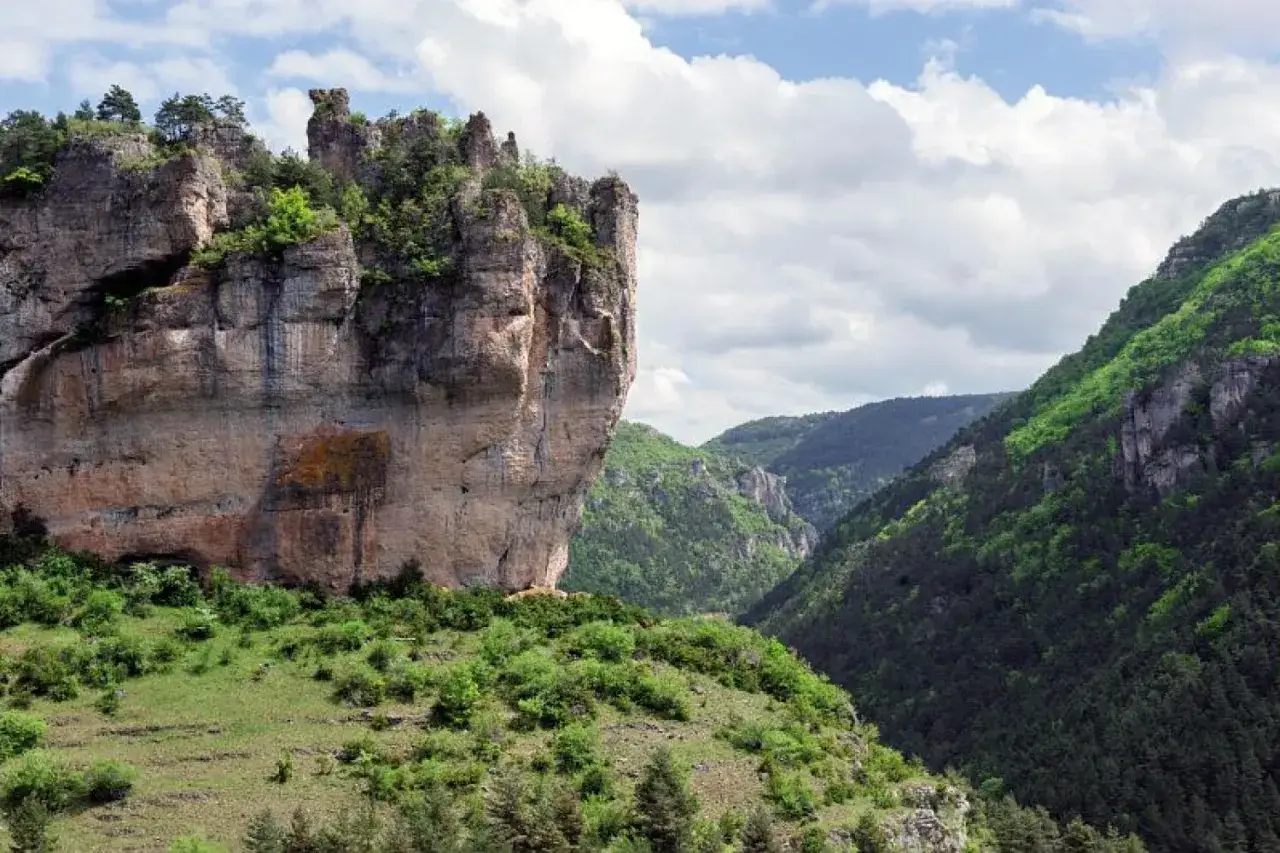 Impressionnante falaise rocheuse dominant une vallée verdoyante, parfaite pour une randonnée sur le Causse Méjean.