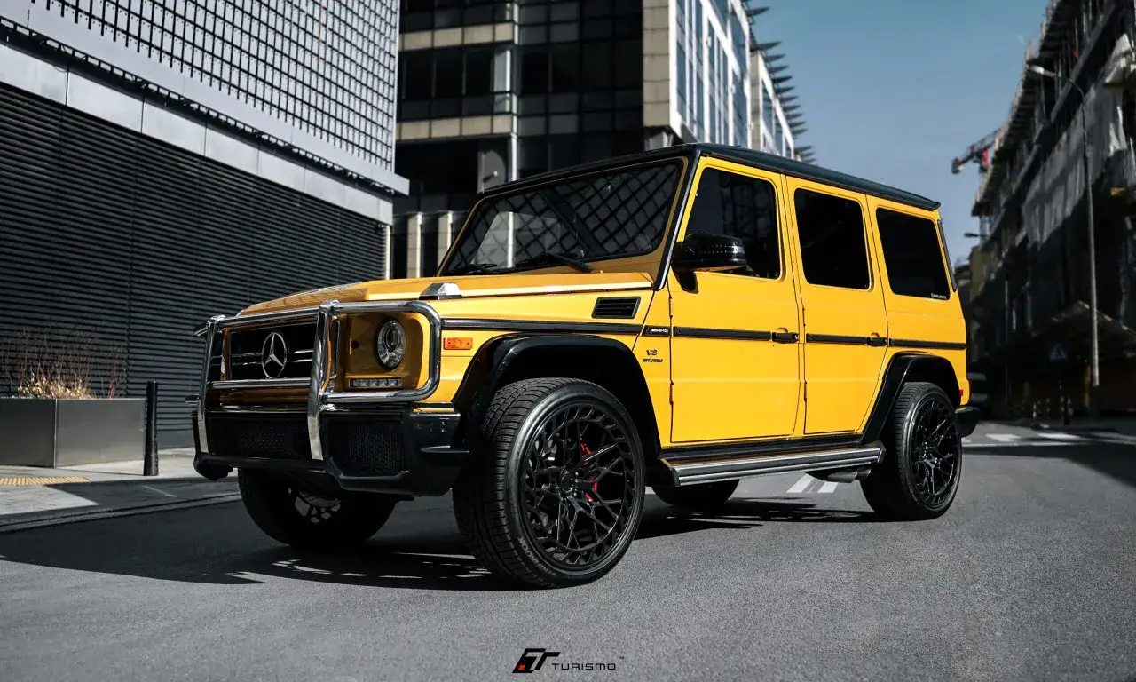 Żółty Mercedes G63 AMG z czarnymi felgami i detalami, zaparkowany na tle nowoczesnych budynków.