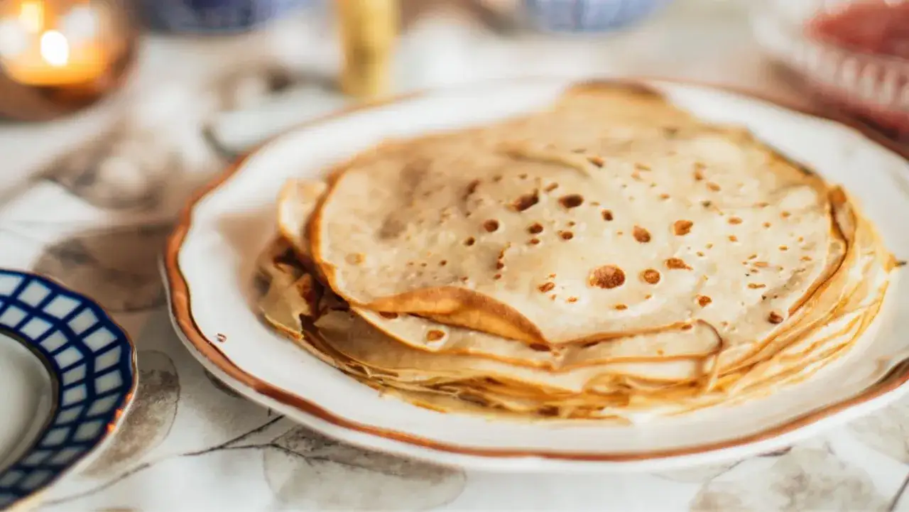 Una pila de crepes dorados y finos en un plato blanco. ¿Qué es crepe? Son perfectos para el desayuno o postre.