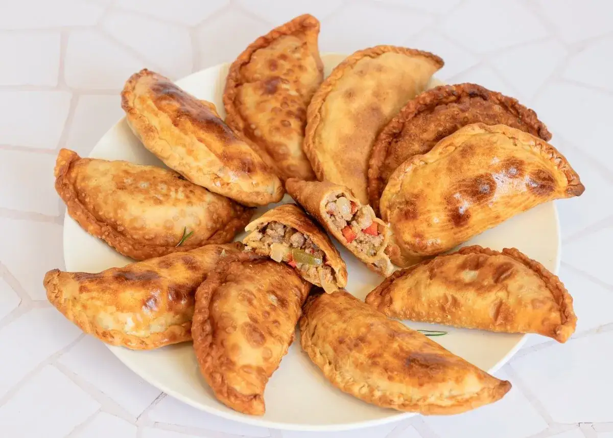 Plato lleno de empanadas de carne doradas y crujientes, una de ellas partida mostrando su sabroso relleno.
