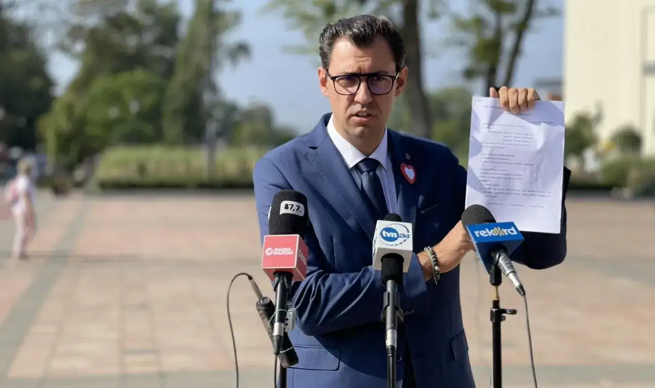 Konrad Frysztak, w garniturze, prezentuje dokumenty przed mikrofonami mediów. Jego wykształcenie i doświadczenie są kluczowe w jego działalności publicznej.