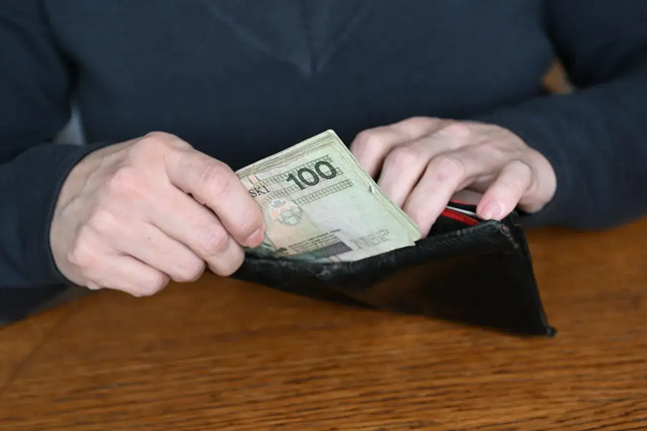 Ręce wkładają do portfela plik banknotów 100 zł. Czy sklejony banknot przyjmą w sklepie?