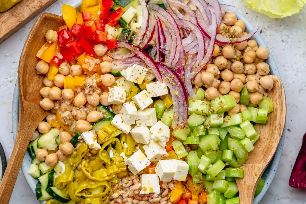 Ensalada mediterr&aacute;nea vibrante con garbanzos, pimientos, pepino, cebolla roja, queso feta y apio, lista para servir.