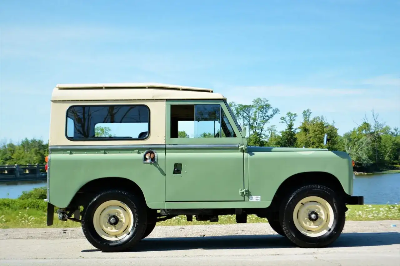 Un cl&aacute;sico Land Rover Santana verde y crema, listo para una aventura junto al lago.