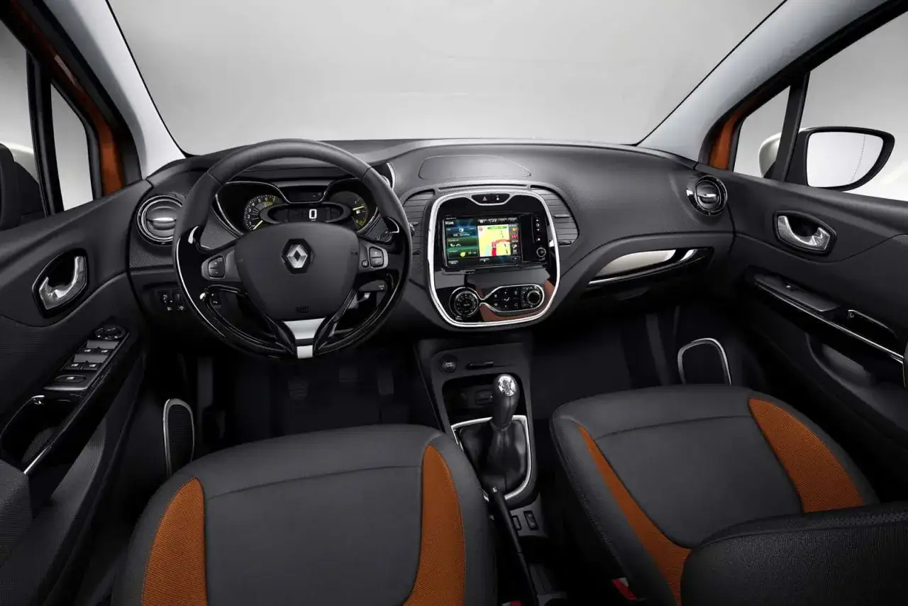 Wnętrze Renault Captur 2015 z ekranem multimedialnym, kierownicą i siedzeniami z pomarańczowymi wstawkami.