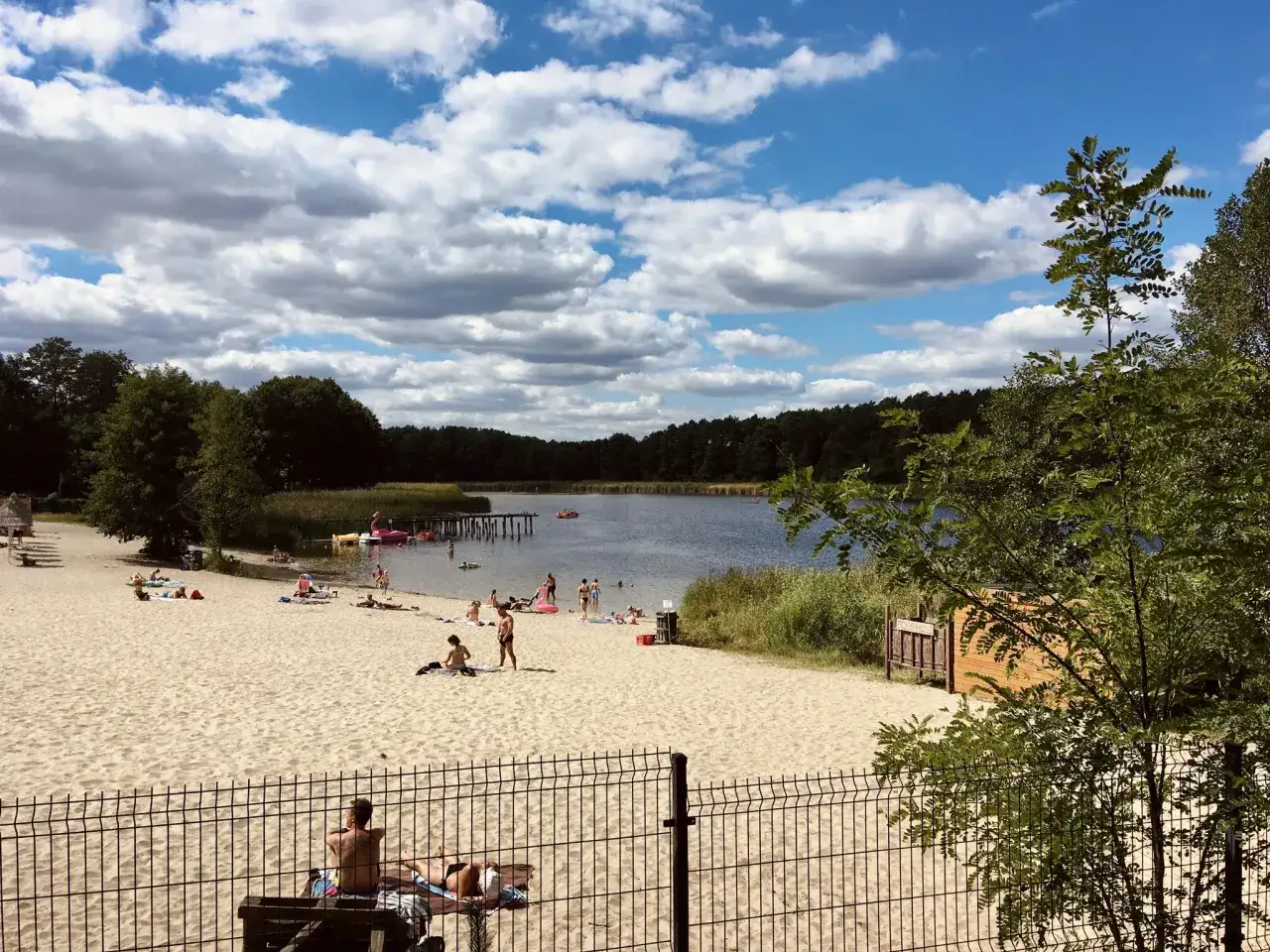 Słoneczna plaża nad jeziorem, ludzie odpoczywają, dzieci się kąpią. Idealne miejsce na wakacje w Złotnikach Kujawskich.