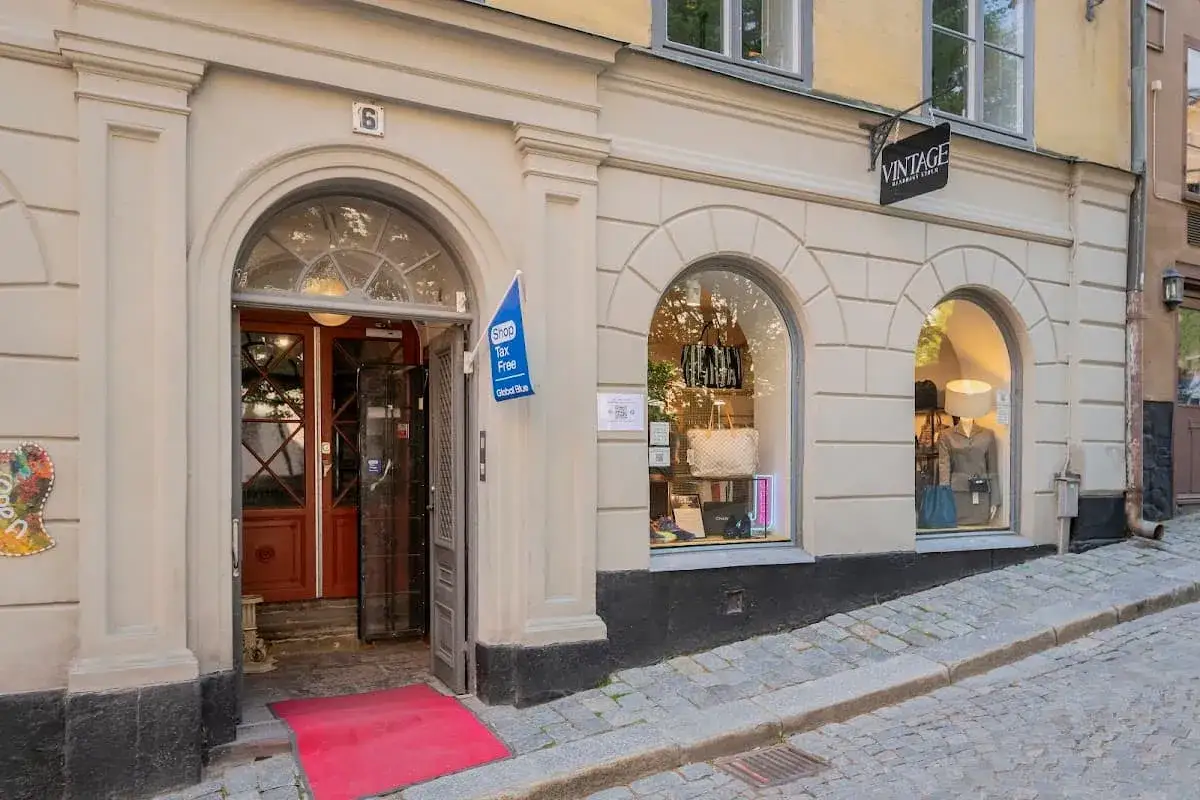 En charmig vintagebutik i Stockholm med en öppen dörr och röda mattan. Fönstren visar upp väskor och kläder, perfekt för en loppisrunda.