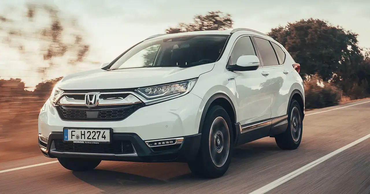 Biała Honda CRV 2025 pędzi po drodze, otoczona rozmazanymi drzewami i słońcem.