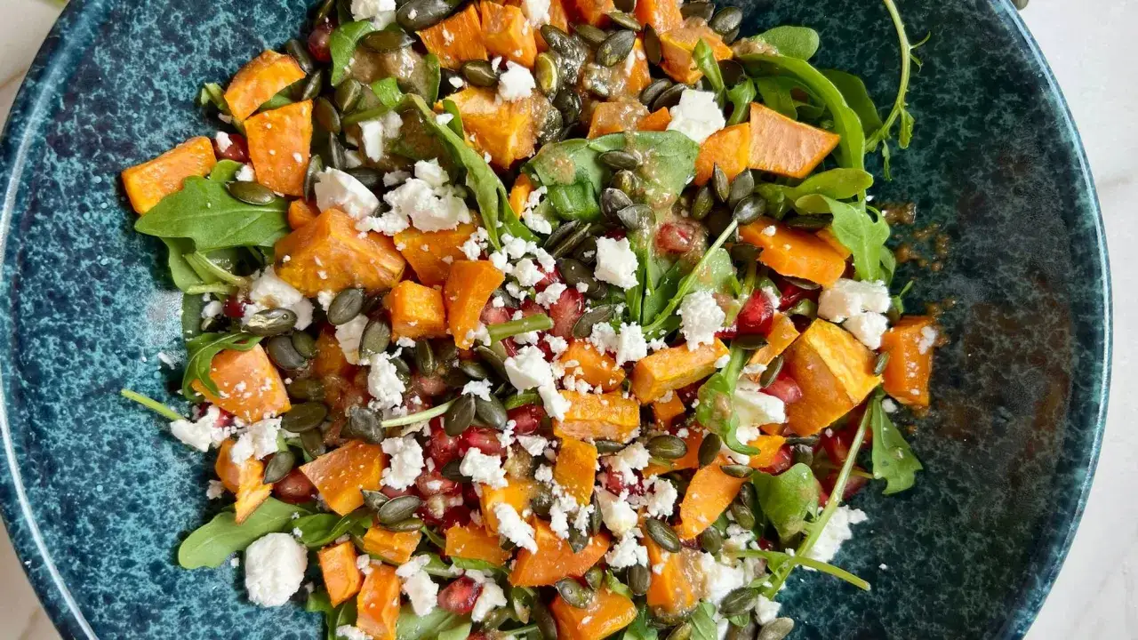 Ensalada de boniato asado con queso feta, granada y semillas de calabaza sobre r&uacute;cula. Un plato vibrante y lleno de sabor.