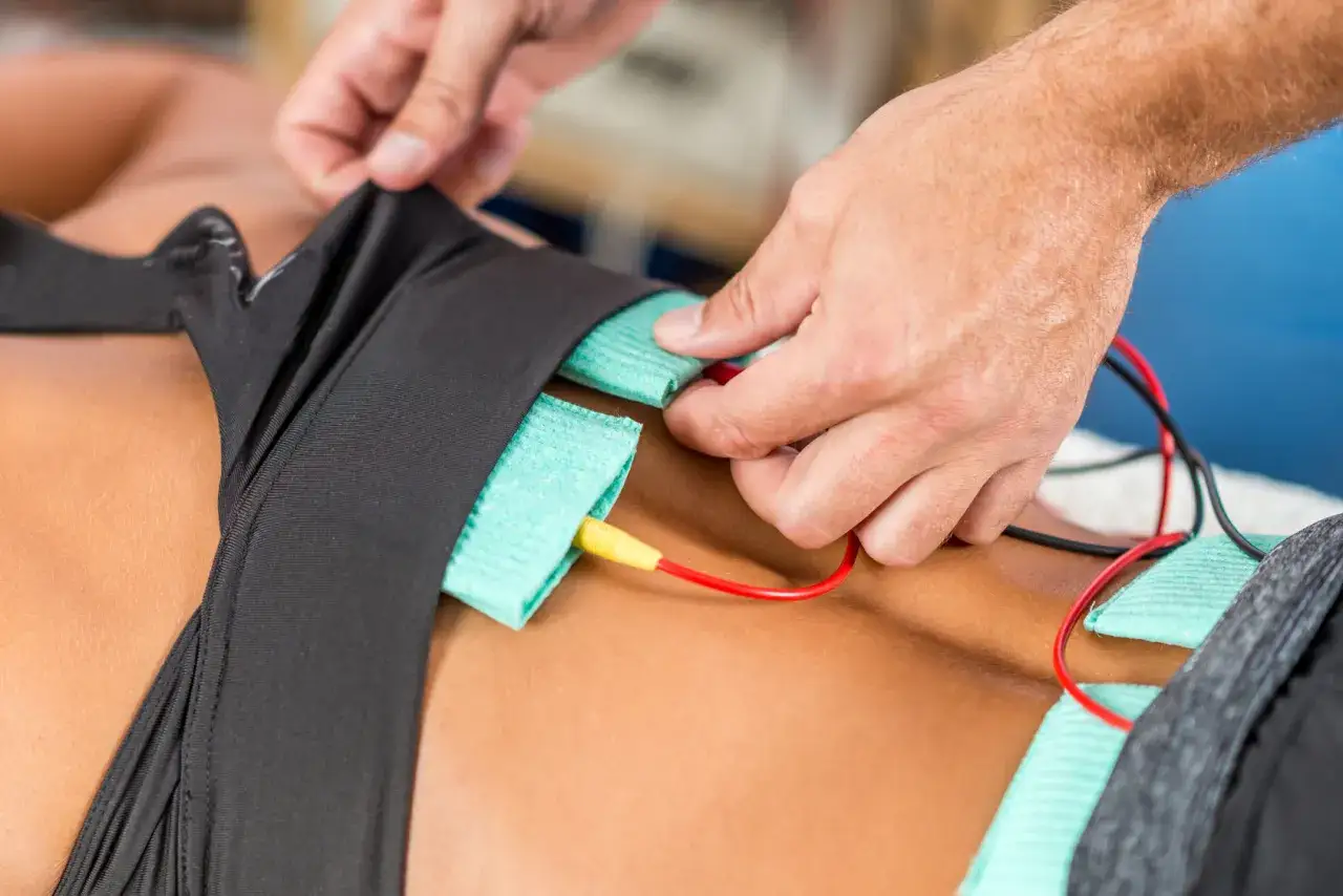 Fizjoterapeuta podłącza elektrody do pasa, przygotowując prądy na kręgosłup lędźwiowy.