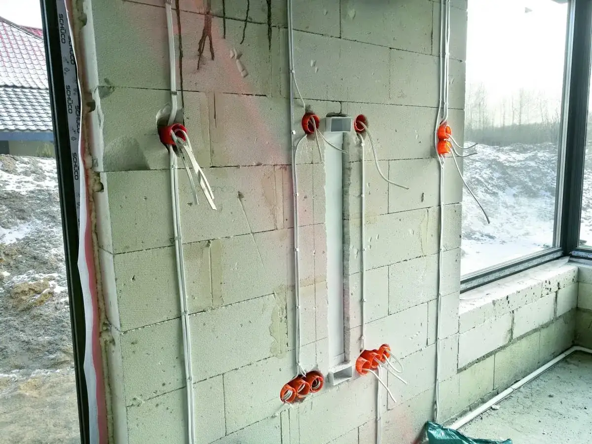 Instalacja elektryczna w ścianie z bloczk&oacute;w betonowych. Widoczne puszki, przewody i peszle. Etap prac wykończeniowych od stanu surowego zamkniętego.