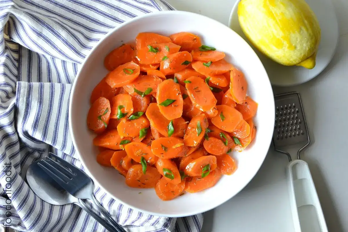 Carote al limone, fresche e saporite, guarnite con erbe aromatiche. Accanto, un limone e una grattugia.