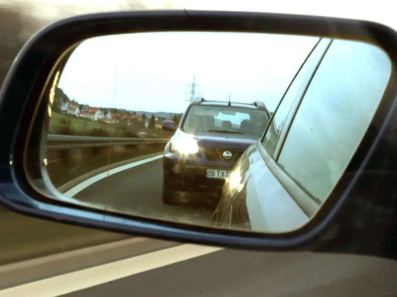 Ein Auto gibt Lichthupe auf der Autobahn. Im R&uuml;ckspiegel ist ein Nissan mit leuchtenden Scheinwerfern zu sehen.