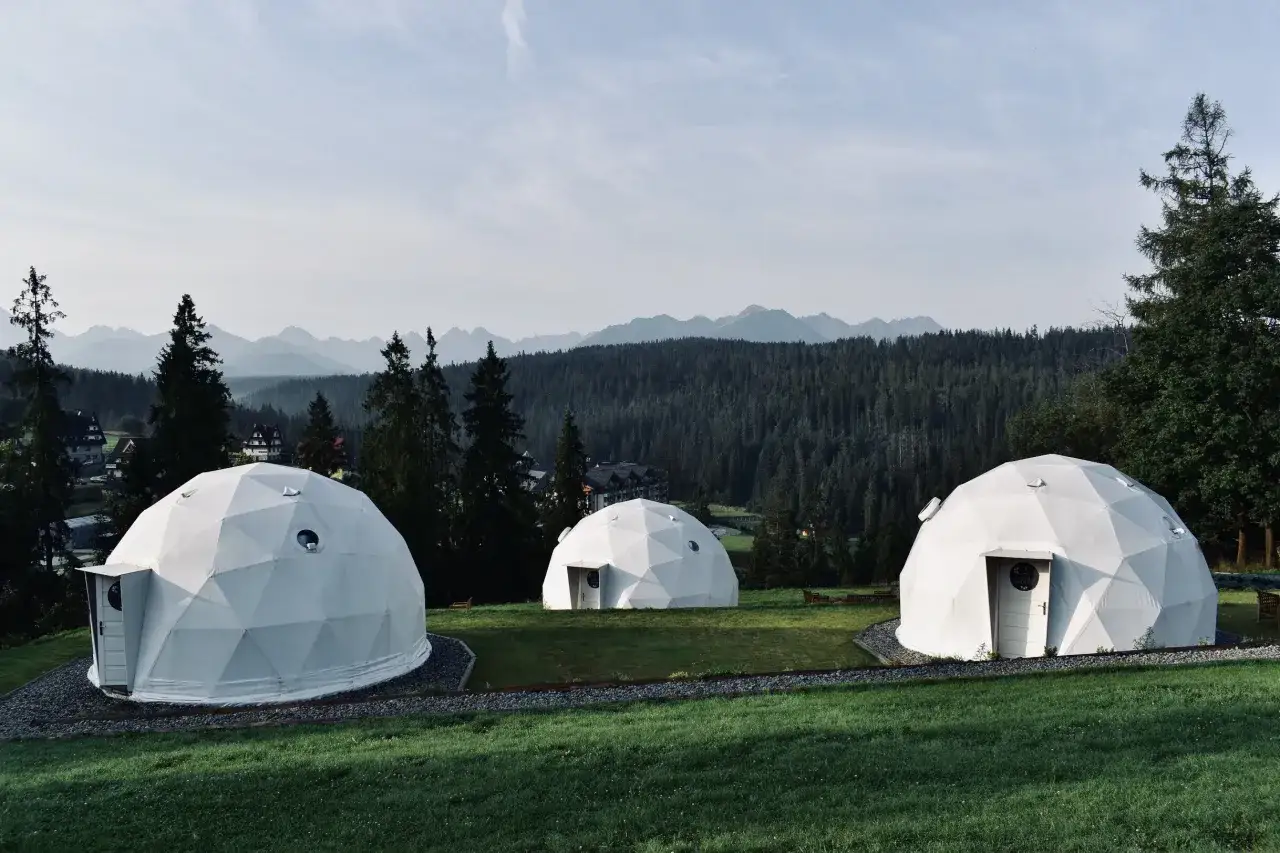 Nowoczesny camping w Tatrach: trzy białe kopuły na tle górskiego lasu i pasma górskiego.