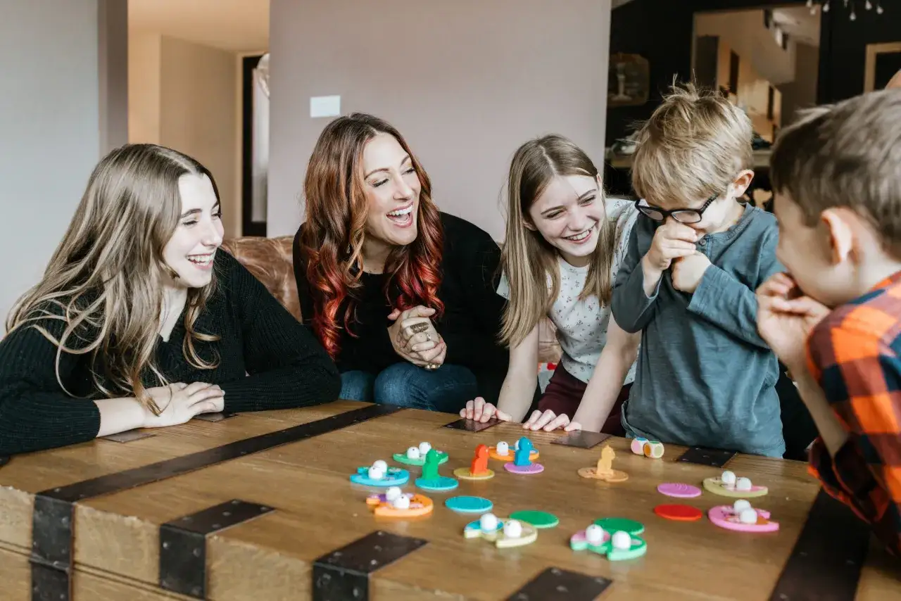 Familia riendo mientras juega un juego de mesa con coloridas piezas. Las preguntas para niños parecen ser el tema.