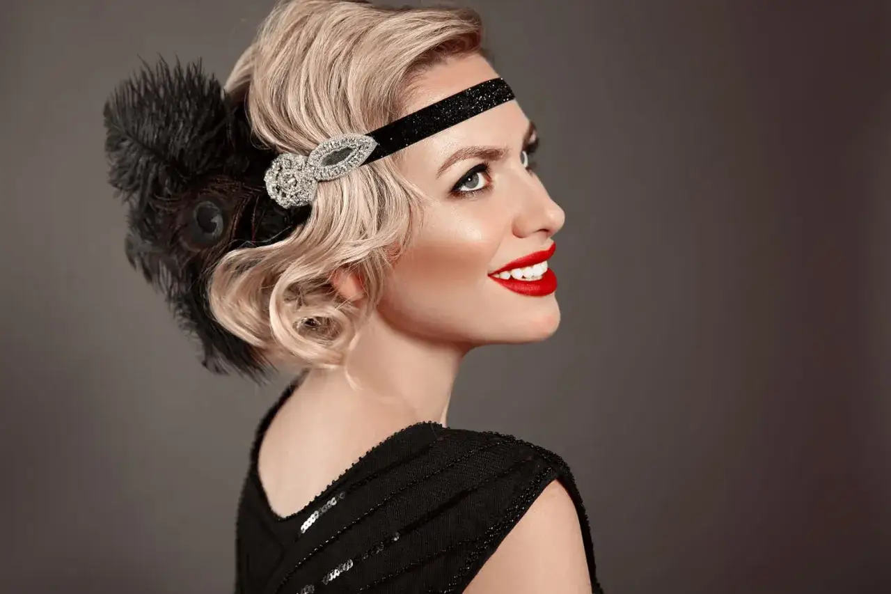 Coiffure année 20 cheveux long, avec bandeau orné de plumes et de strass. Rouge à lèvres éclatant.