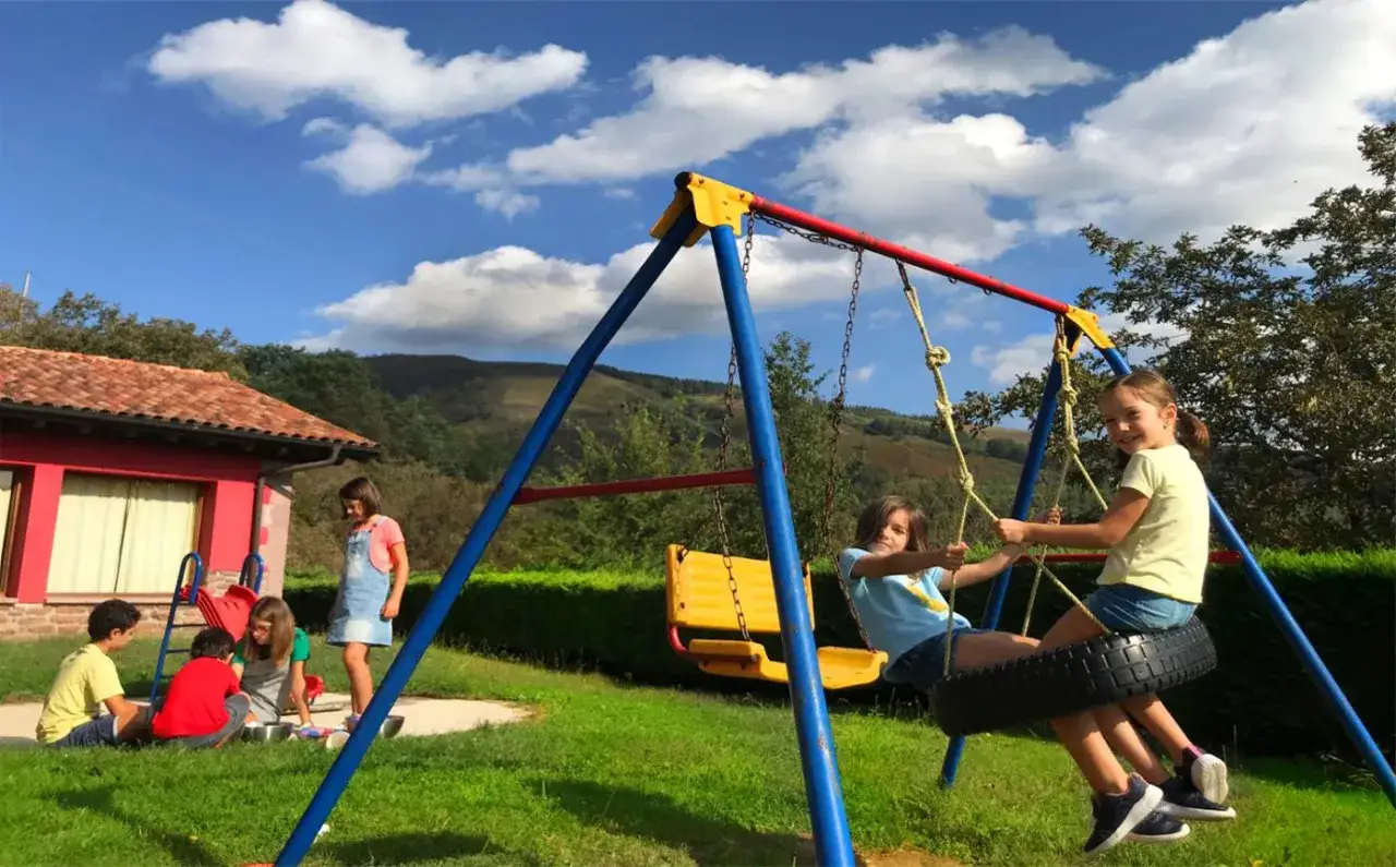 Niños jugando en un columpio y en el suelo, un día perfecto para saber qué hacer en familia al aire libre.