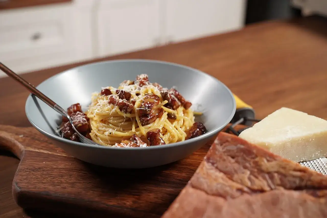 Pyszne spaghetti carbonara, idealne danie, by dowiedzieć się, co zjesc w Rzymie. Obok kawałek parmezanu i guanciale.