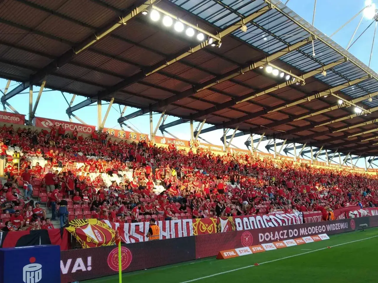 Tłum kibiców w czerwonych barwach na trybunach stadionu, gotowy do emocjonującego derby łodzi.