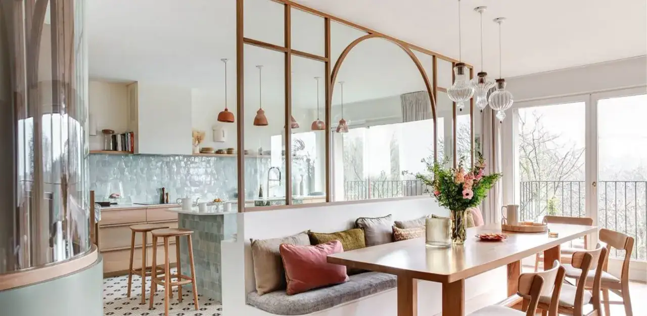 Un élégant **modèle de cuisine ouverte** avec un îlot central, des banquettes confortables et une table à manger, séparés par une verrière stylisée.