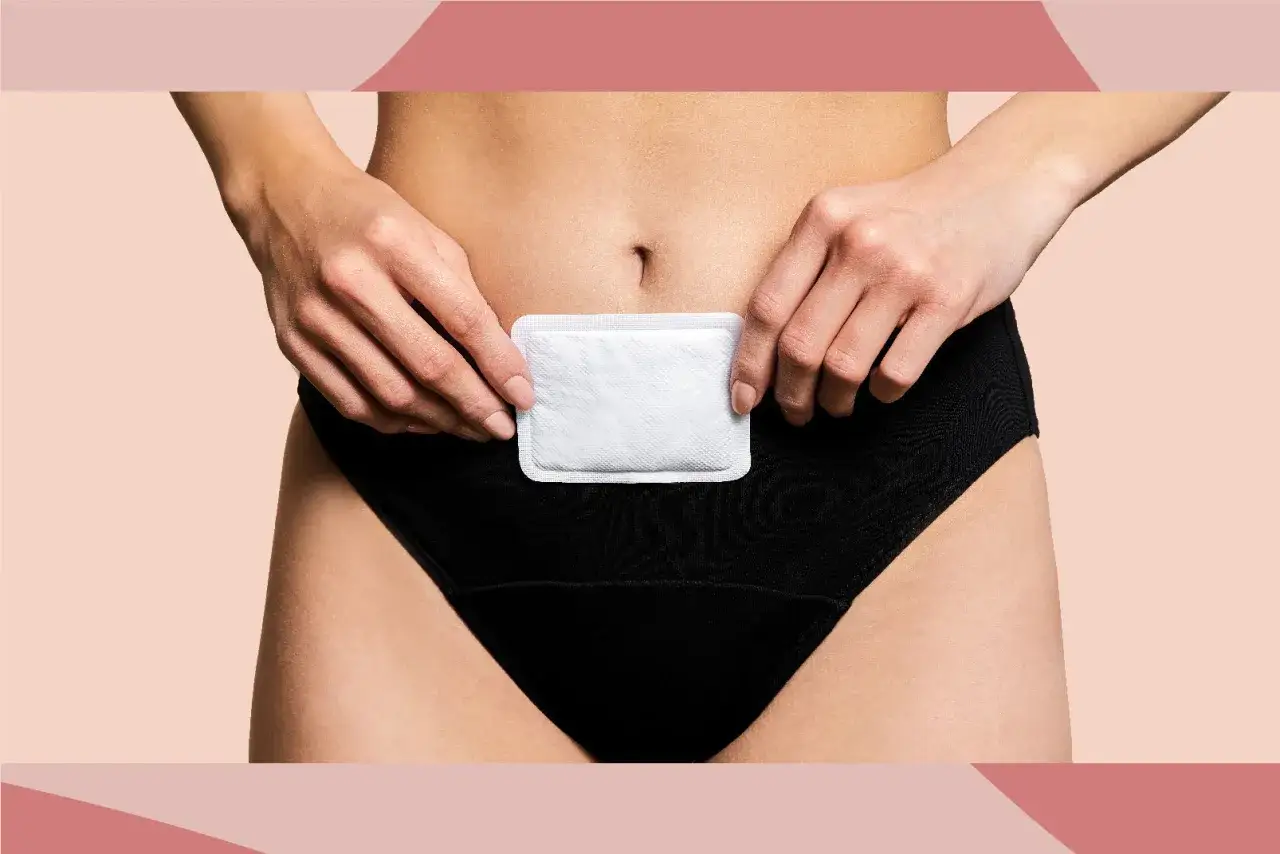 Alivio para el dolor regla. Una mujer aplica un parche térmico en su abdomen bajo para calmar las molestias.