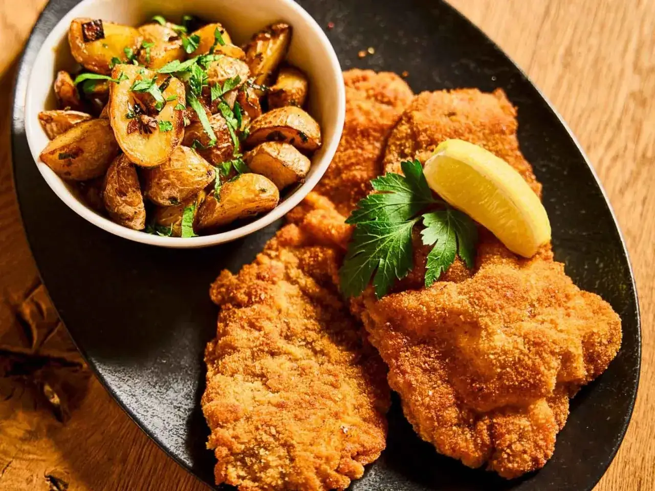 Knuspriges Schnitzel mit Bratkartoffeln, Zitrone und Petersilie &ndash; ein Klassiker, der in Berlin immer schmeckt.