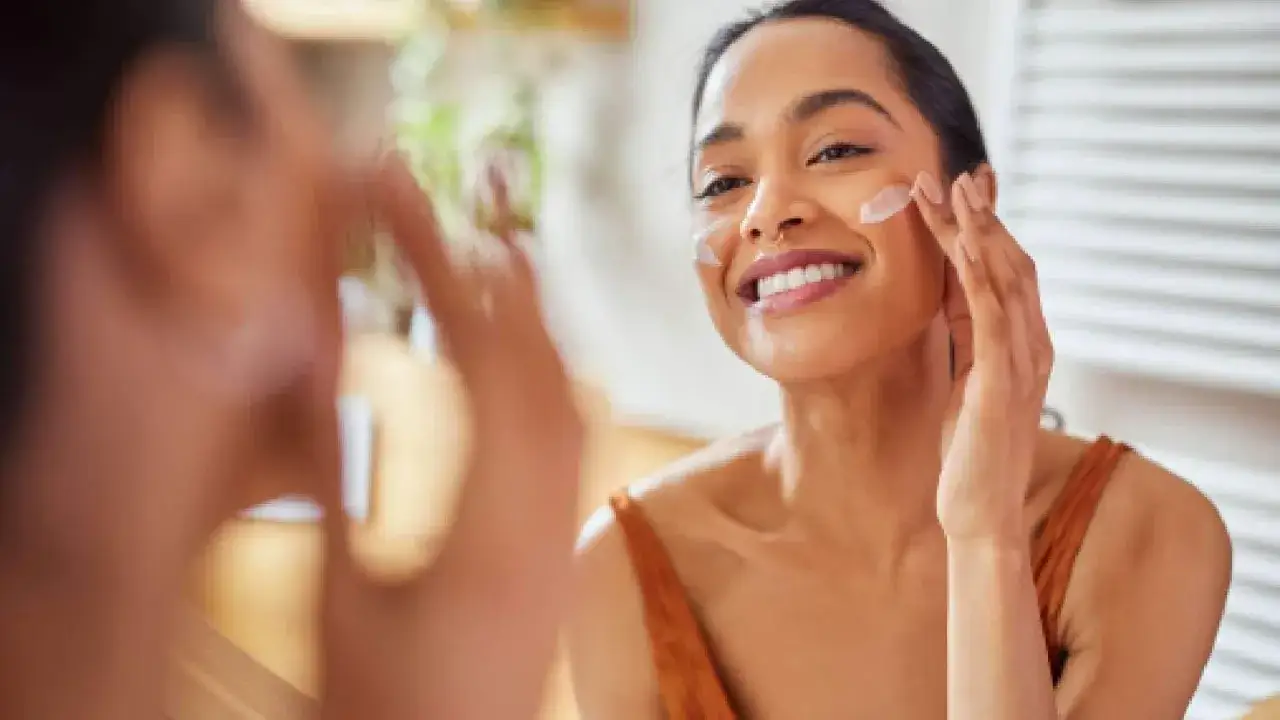 Une femme souriante applique de la crème sur son visage, un geste simple pour comment appliquer crème visage.